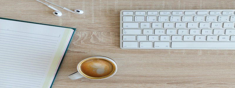 A cup of coffee, notebook, and keyboard on the table
